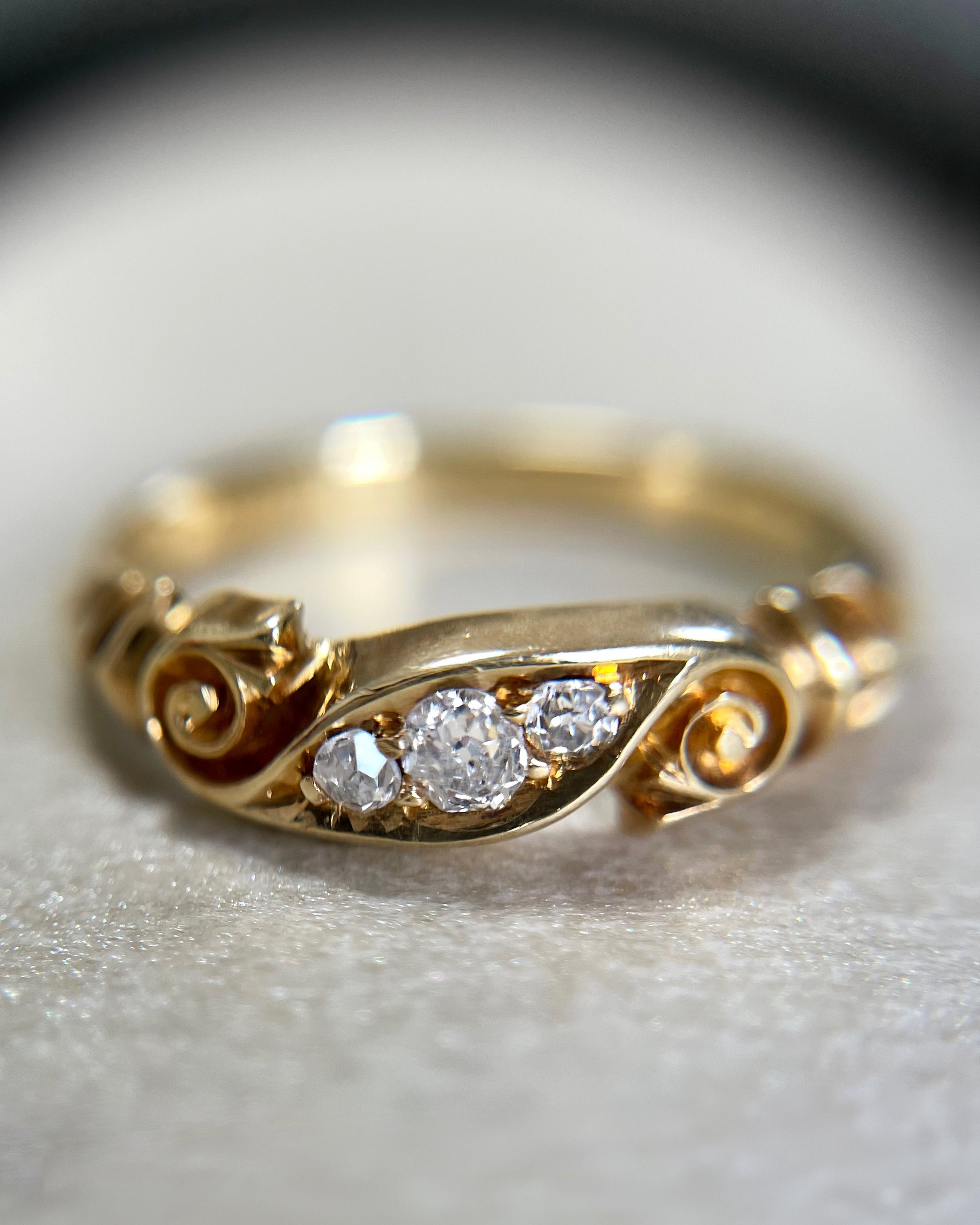 Close-up of Victorian 18kt gold three stone diamond ring showing old mine cut diamonds and carved banner detail – Auric Vintage