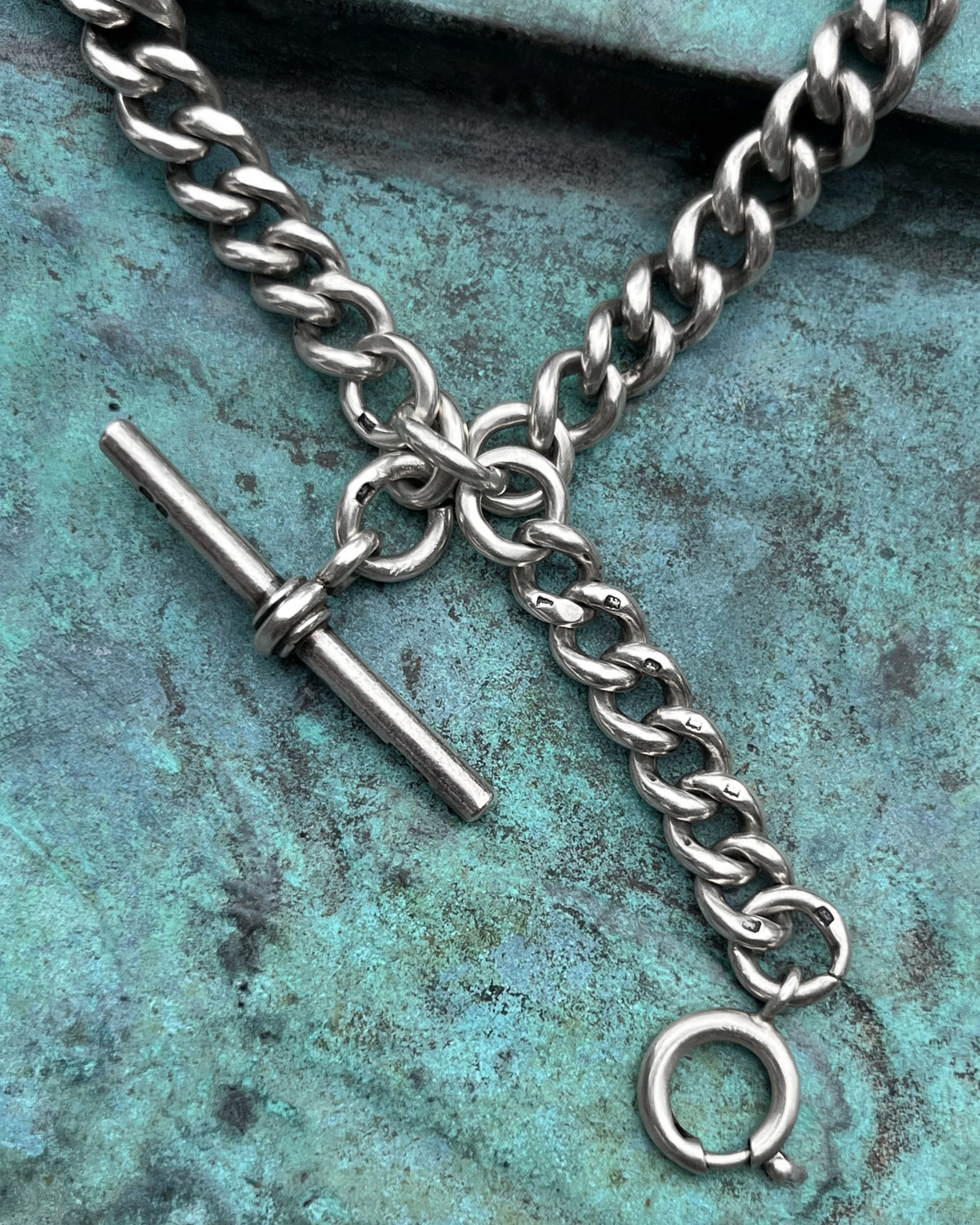 Close-up of the antique Sterling silver T-bar and additional pendant drop on a watch chain, showing the swivel clasp and curb links.