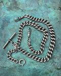 Antique Sterling silver watch chain with graduated puffy curb links, T-bar and swivel clasps, shown against a green bronze background.