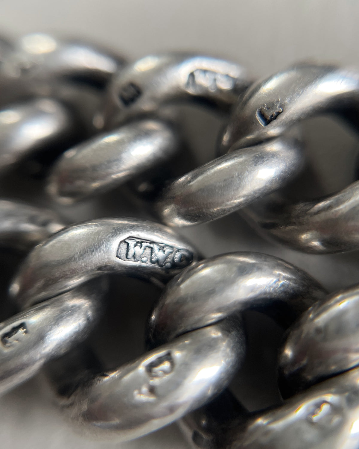 Close-up of the individual curb links on an antique Sterling silver watch chain, showing the lion passant hallmarks stamped into each link.