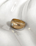 1970s French vintage 18kt yellow gold diamond solitaire engagement ring with round brilliant cut diamond, shown from the side on a white undulating tile