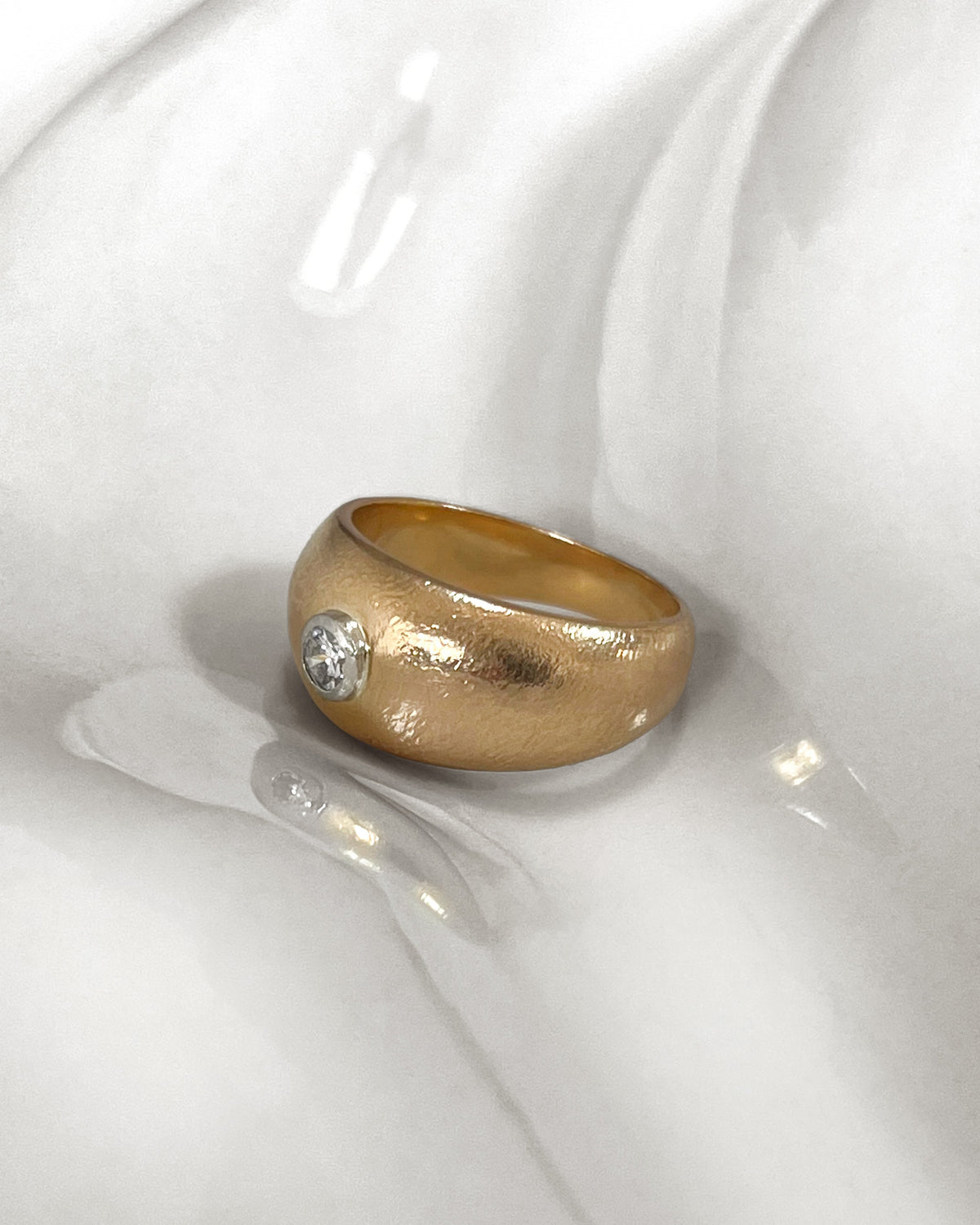 1970s French vintage 18kt yellow gold diamond solitaire engagement ring with round brilliant cut diamond, shown from the side on a white undulating tile