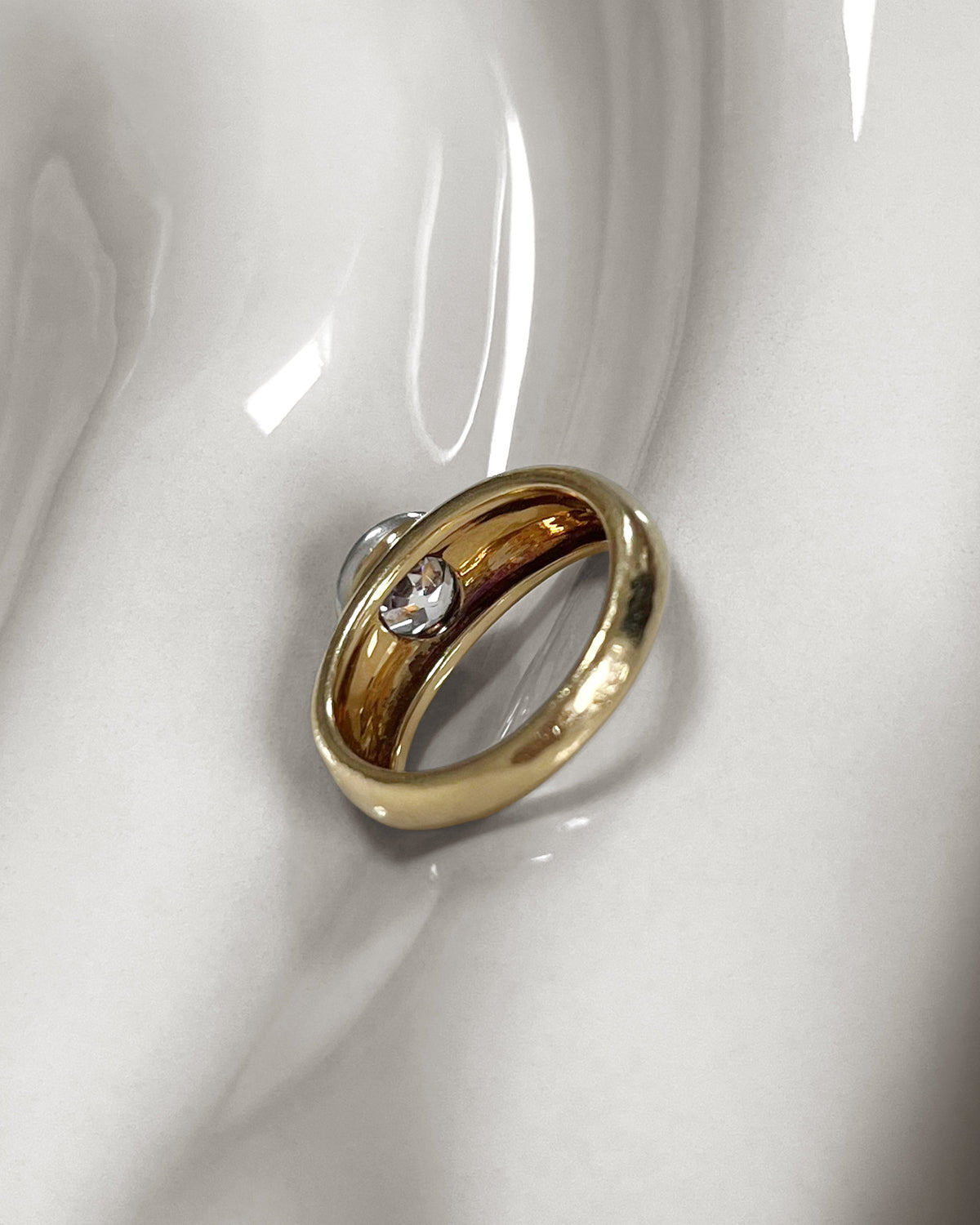 Reverse of vintage diamond solitaire engagement ring showing the broad rounded shoulders tapering towards the back, on an undulating white tile.