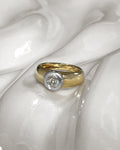 Vintage diamond solitaire engagement ring with approximately 0.60ct warm L/M colour Old Mine cut diamond in a chunky platinum bezel setting, shown on an undulating white tile.