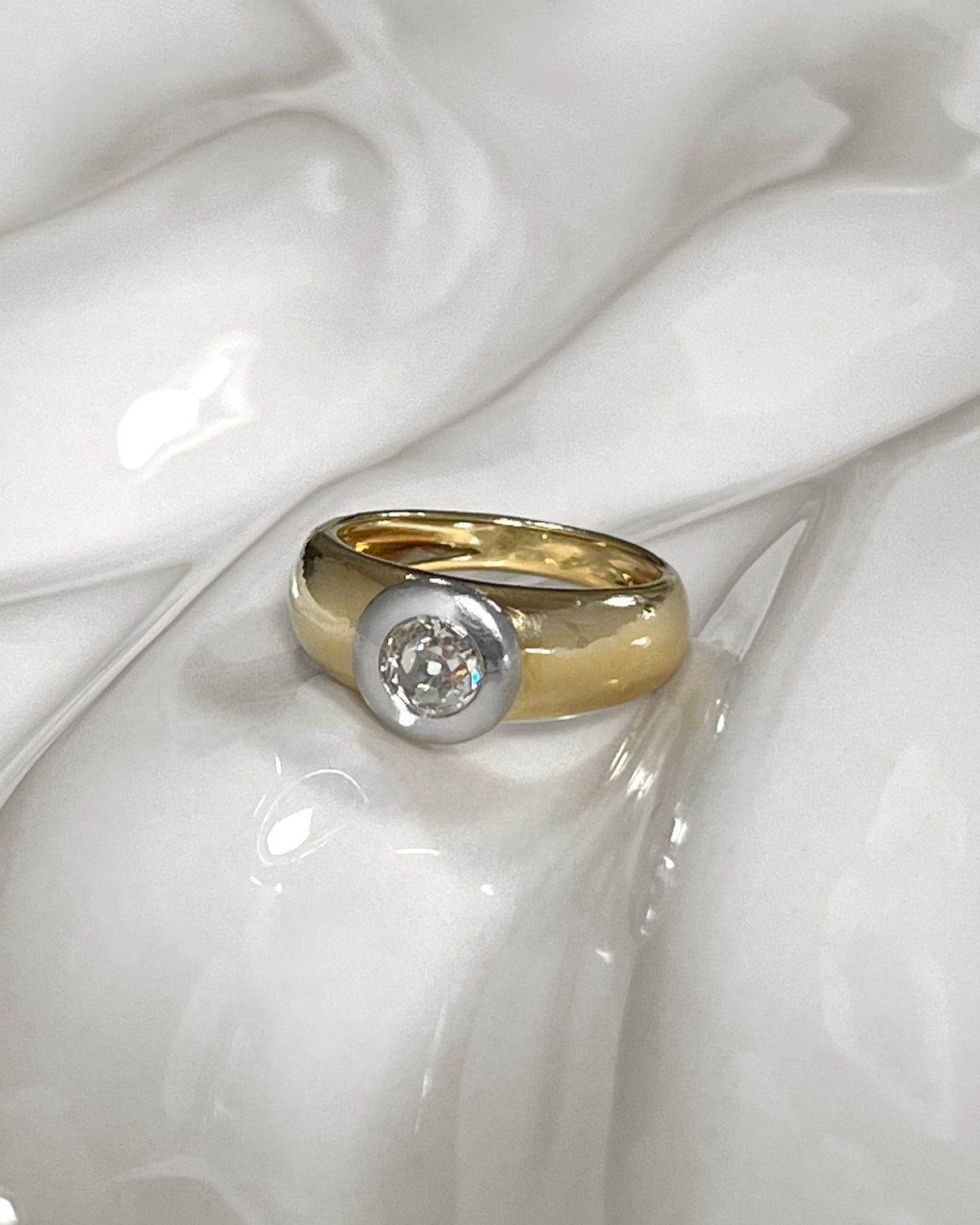Vintage diamond solitaire engagement ring with approximately 0.60ct warm L/M colour Old Mine cut diamond in a chunky platinum bezel setting, shown on an undulating white tile.