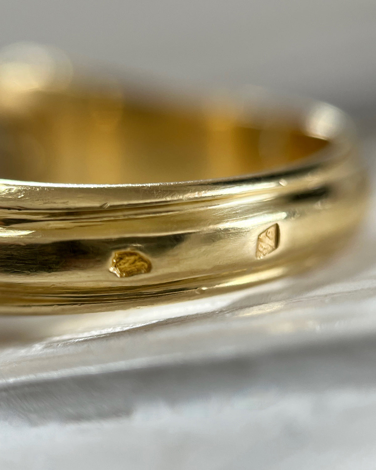 Close-up of the French hallmarks and maker's mark on a 1990s vintage 18kt two-tone gold diamond solitaire engagement ring, viewed through a jeweller's loupe.