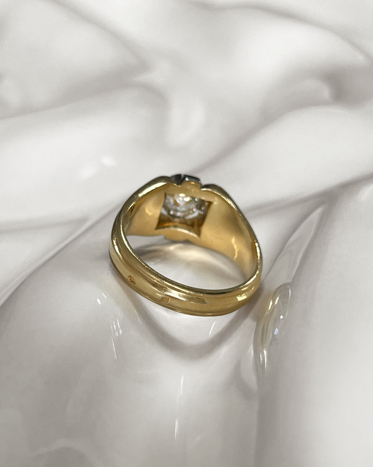 Reverse of 1990s vintage 18kt two-tone gold diamond solitaire engagement ring, showing the tapering yellow and white gold shoulders on an undulating white tile.