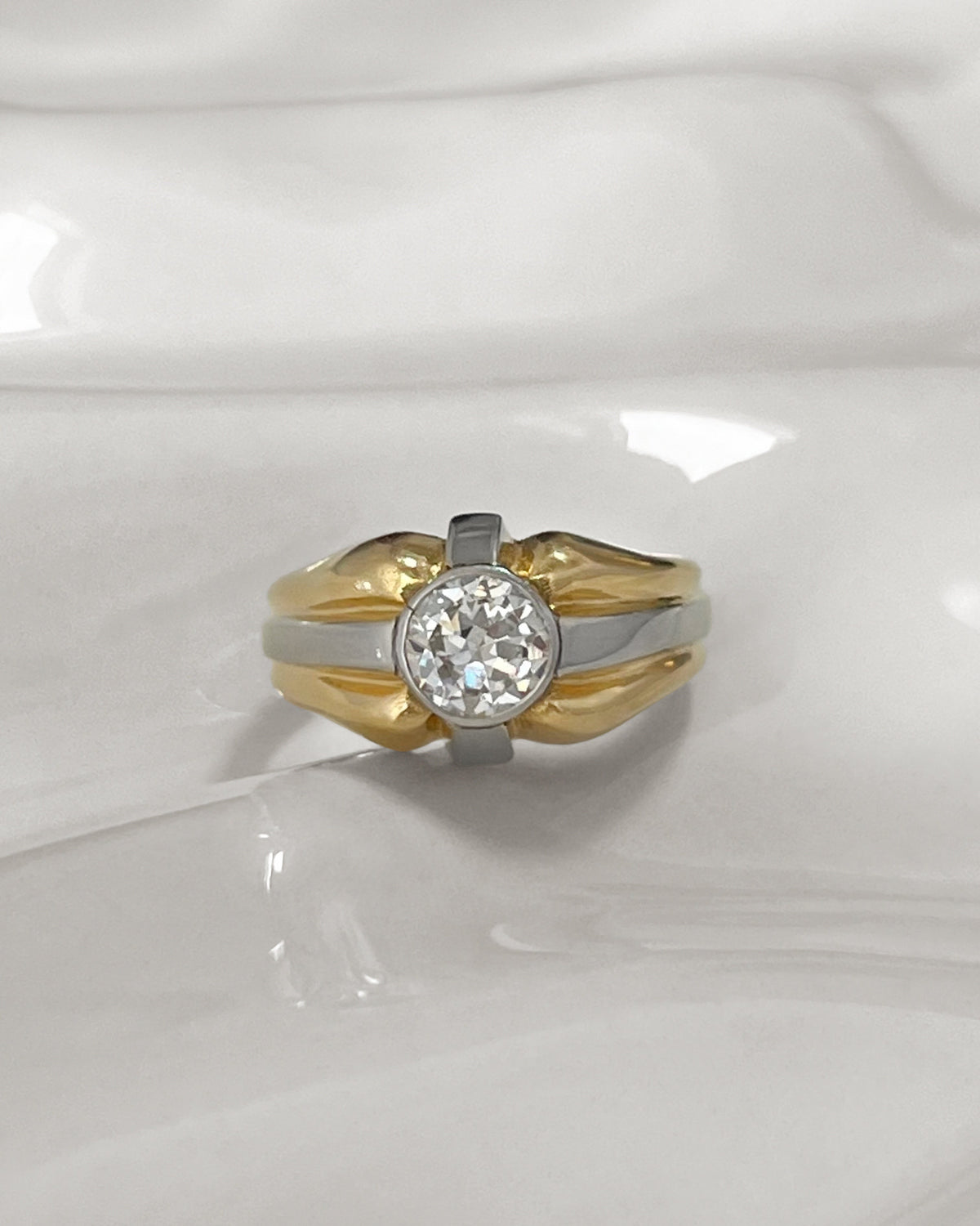 1990s vintage 18kt two-tone gold diamond solitaire engagement ring with a 0.90ct Old European cut diamond in a platinum millegrain setting, shown on an undulating white tile.