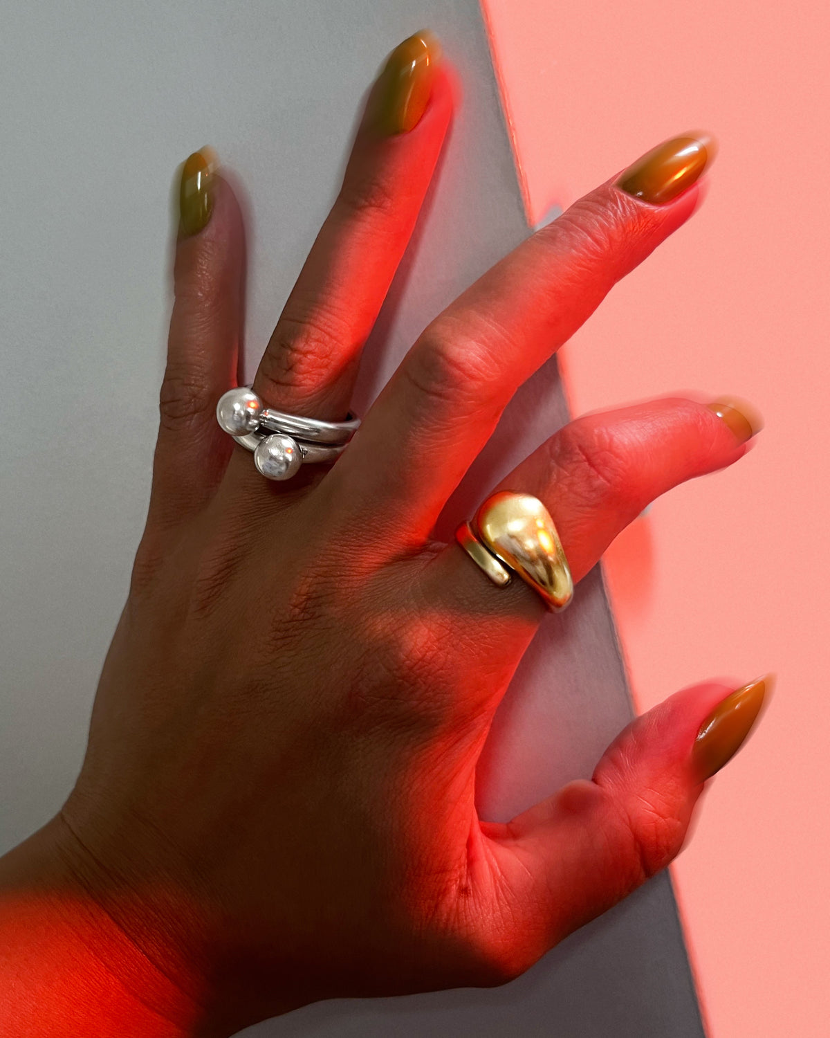 Vintage 18kt gold sculptural coil ring worn on a hand alongside silver rings, against a white wall with red light.