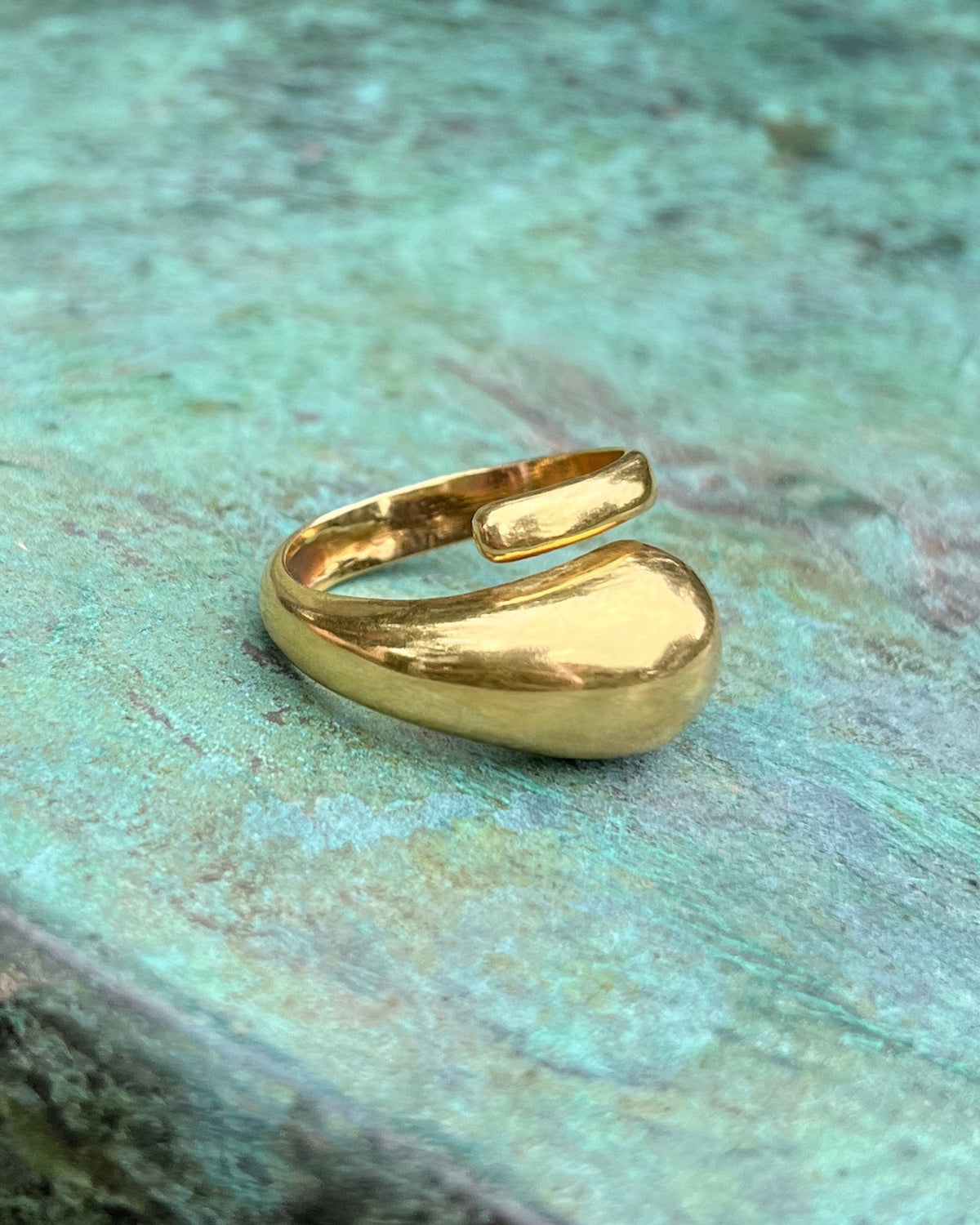 Side view of a vintage 18kt gold asymmetric coil ring showing the curved sculptural form and polished domed end, against a green bronze background.