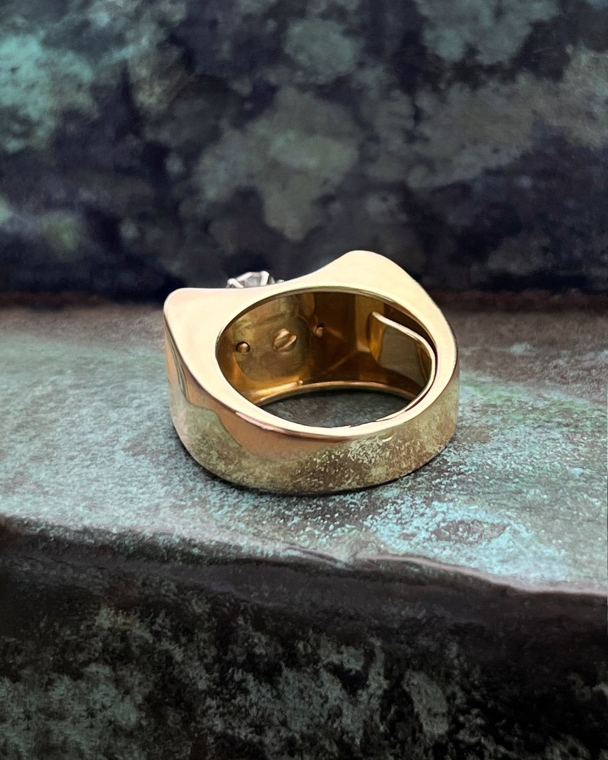 Reverse view of a 1940s vintage tank ring showing the bold curved dome and polished gold surface against a green bronze background.