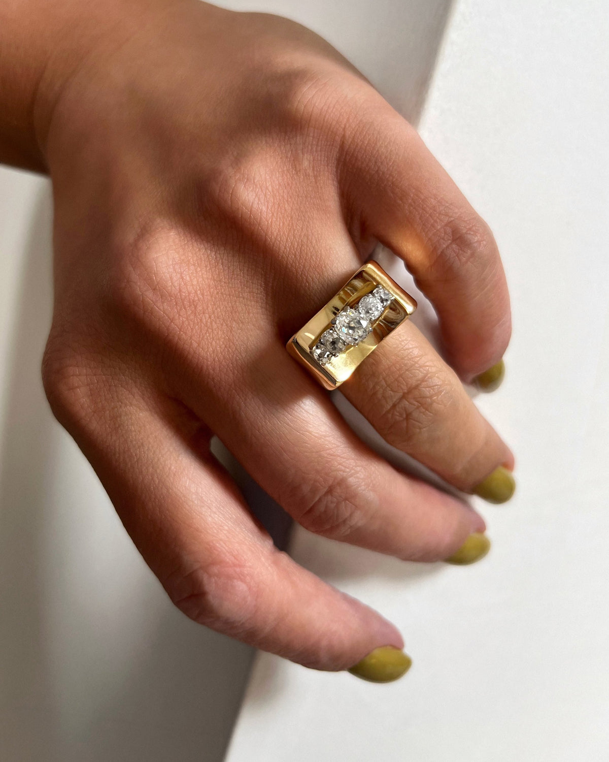 1940s vintage tank ring set with five graduating Old Mine cut diamonds in four-claw settings, shown on a hand against a white wall.

