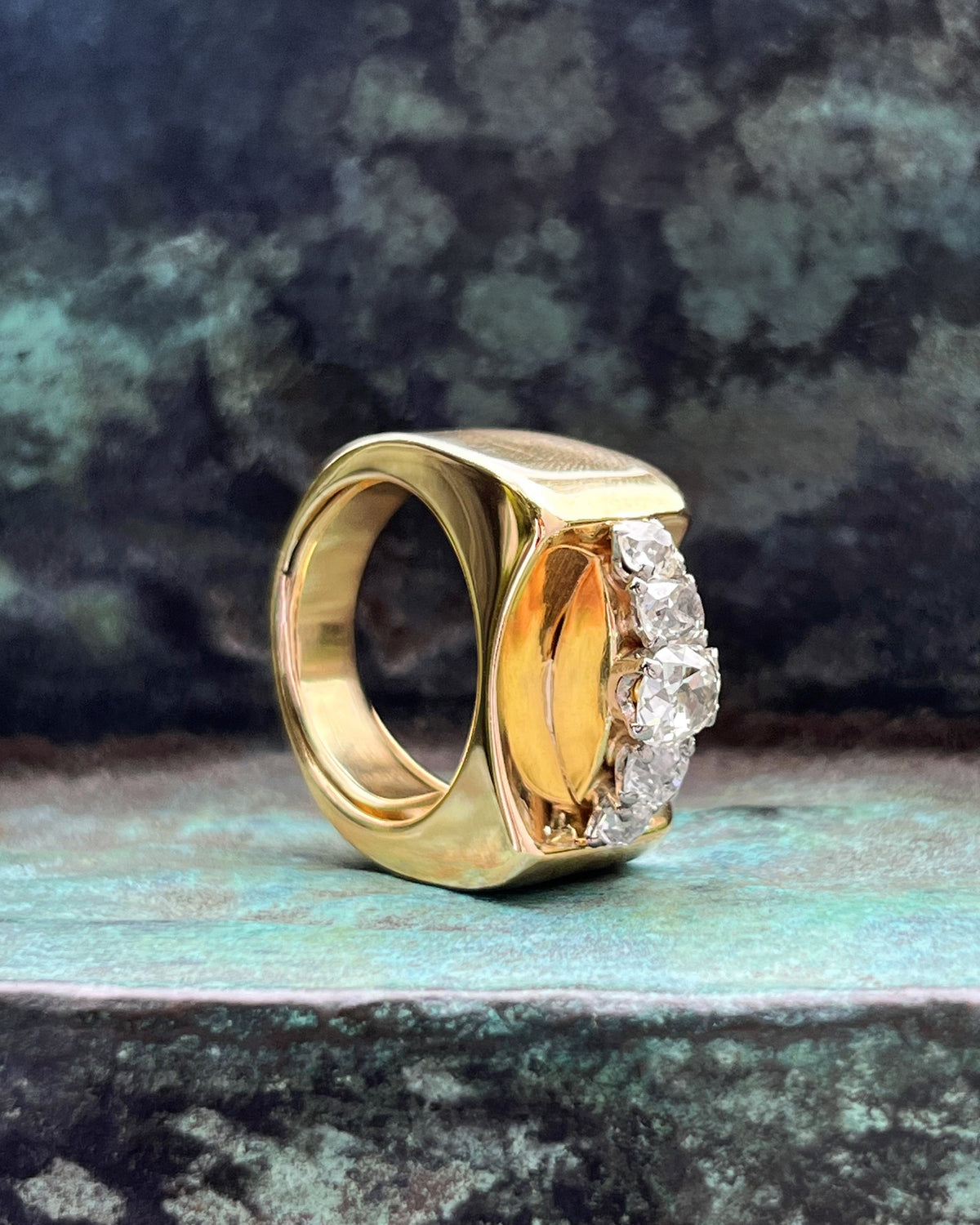Side view of a 1940s vintage diamond tank ring showing the curved domed setting and polished modernist surfaces, against a green bronze background.