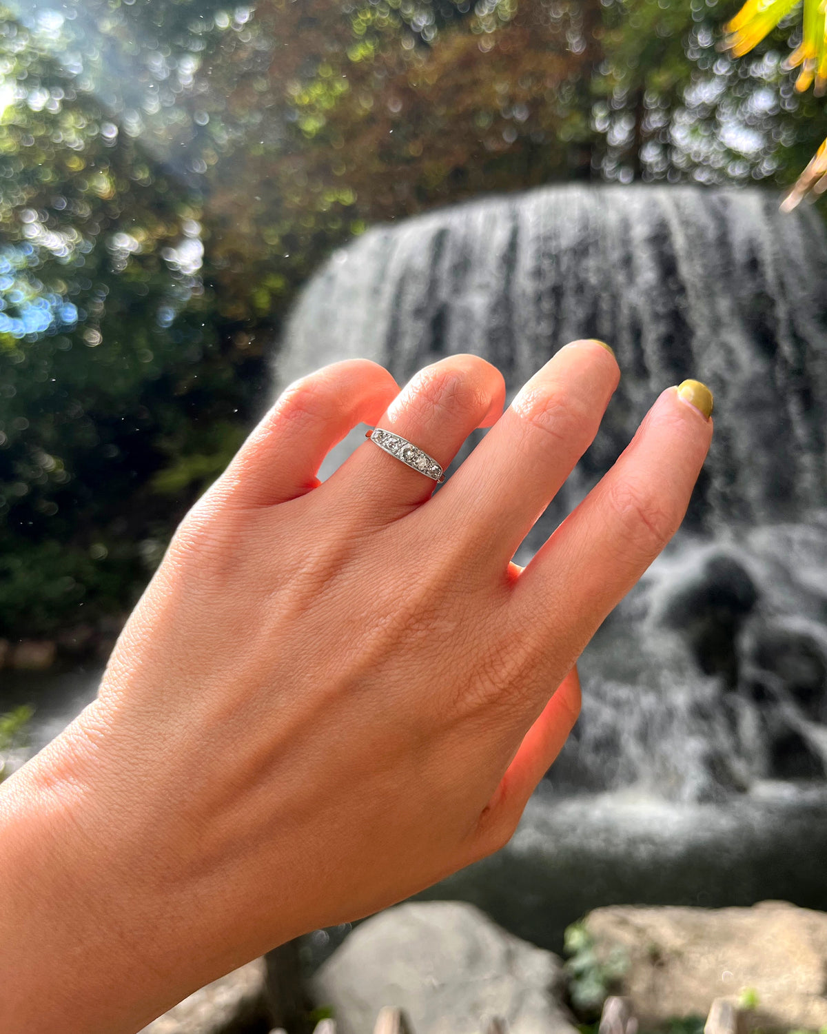 Antique five-stone diamond ring with five graduating cushion-shaped Old Mine cut diamonds in fine millegrain platinum borders, shown on a hand with a waterfall in the background.