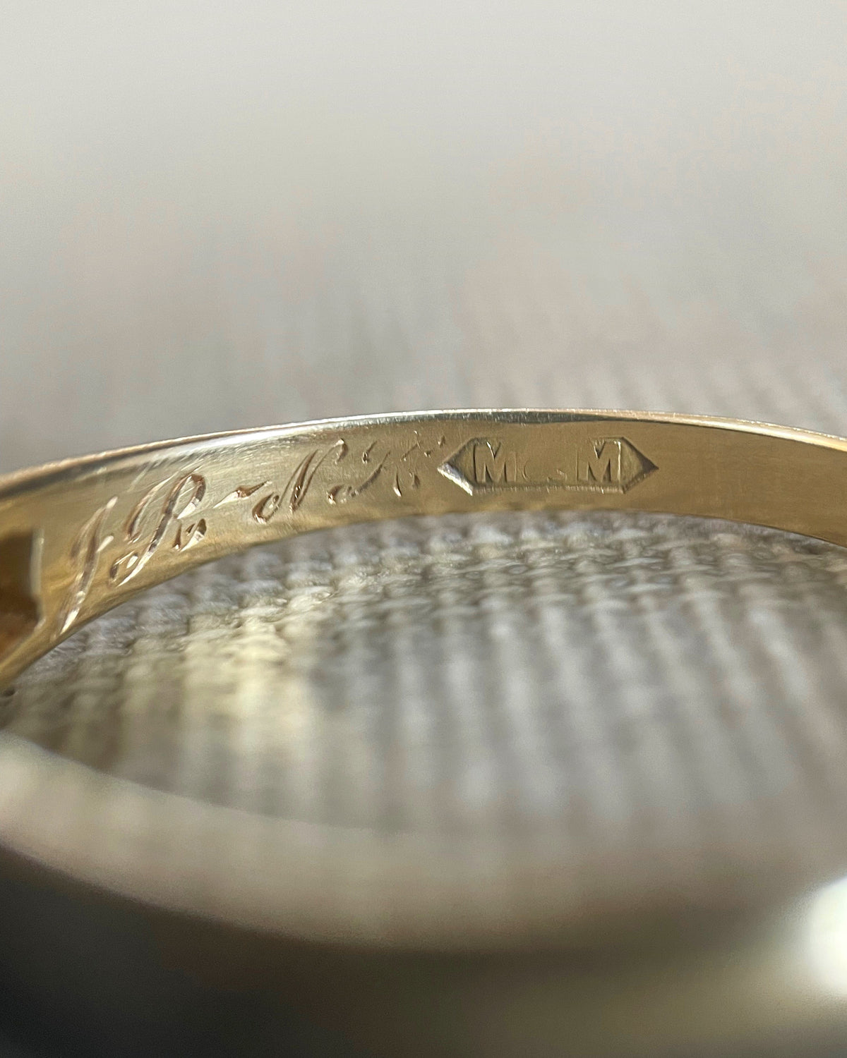 Close-up of the engraved initials “J.R-N.K” inside an antique Victorian 18kt gold navette ring, viewed in detail.