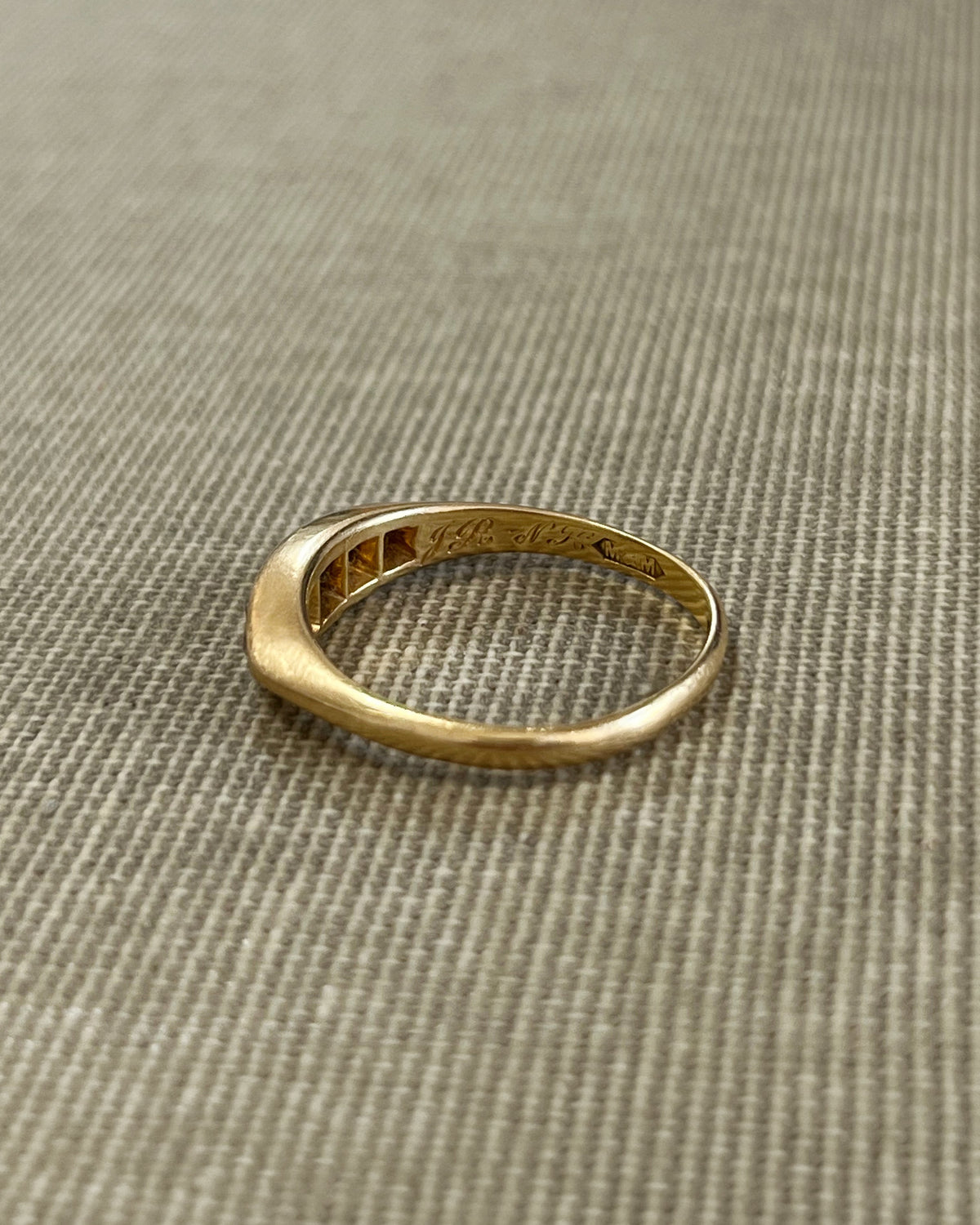 Side view of an antique Victorian 18kt gold navette ring showing the curved boat-shaped setting and row of diamonds, against textured beige canvas.