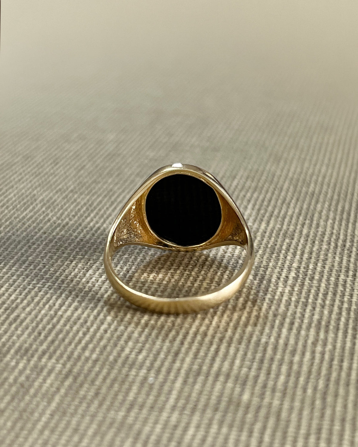 Reverse view of a vintage 9kt gold oval signet ring showing the smooth gold shank and rubover setting around the black onyx.