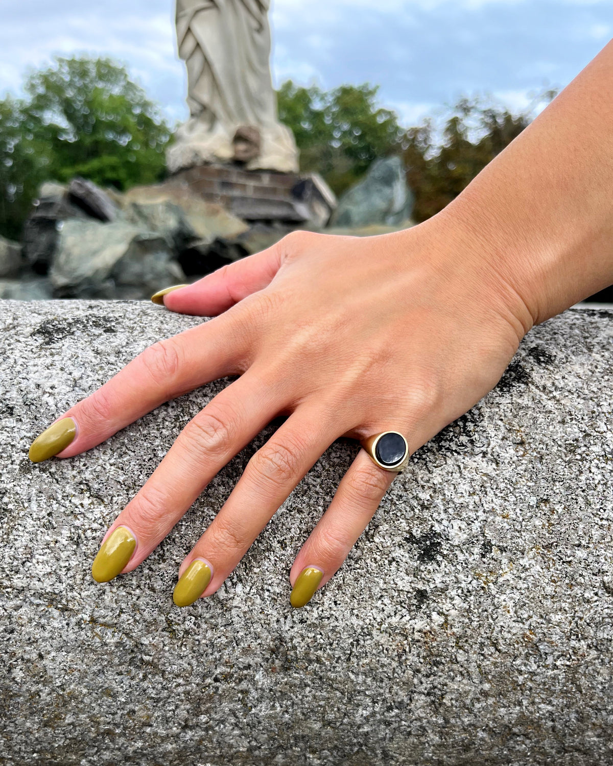 Vintage 9kt gold oval signet ring with polished black onyx tablet, shown worn on a pinky finger beside a fountain.