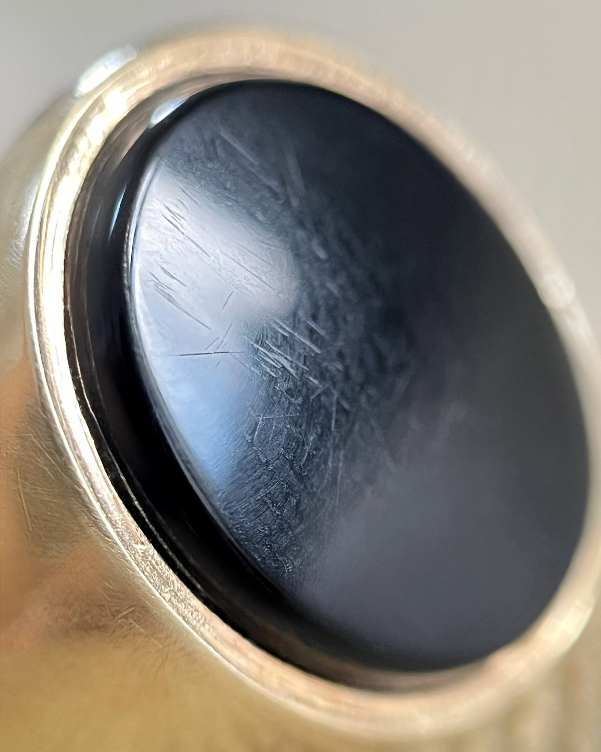 Magnified close-up of the polished black onyx tablet in a vintage 9kt gold signet ring, showing the smooth rubover setting.
