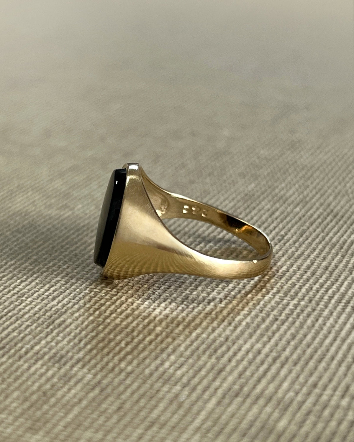 Side view of a vintage 9kt gold oval signet ring showing the broad architectural shoulders tapering towards the shank, against a beige canvas background.