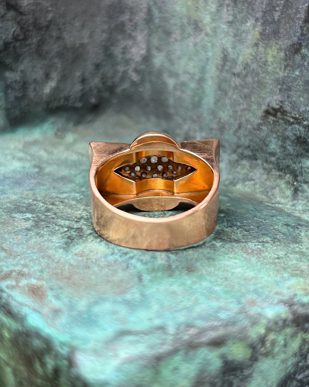 Reverse view of a 1940s vintage tank ring showing the angular chevron form and polished gold surface against a green bronze background.