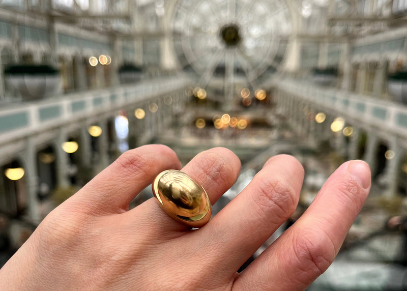 Bvlgari 18kt gold ring on a hand in front of a blurred indoor architectural background, of Stephen's Green Shopping Centre, a vintage Dublin Landmark.