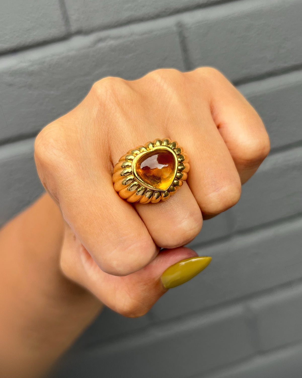 Vintage chunky 18kt gold statement ring with a heart-shaped golden citrine cabochon and ribbed detailing, shown on a hand against a grey wall.