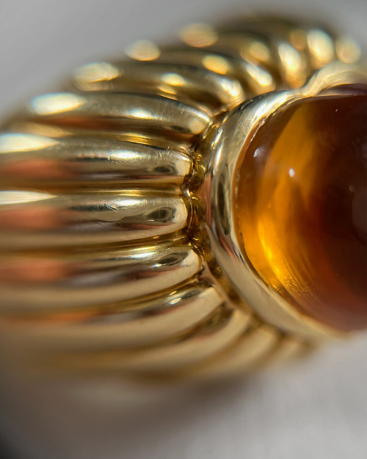 Magnified side view of a vintage 18kt gold citrine statement ring showing the raised heart-shaped cabochon and radiating ribbed gold frame.