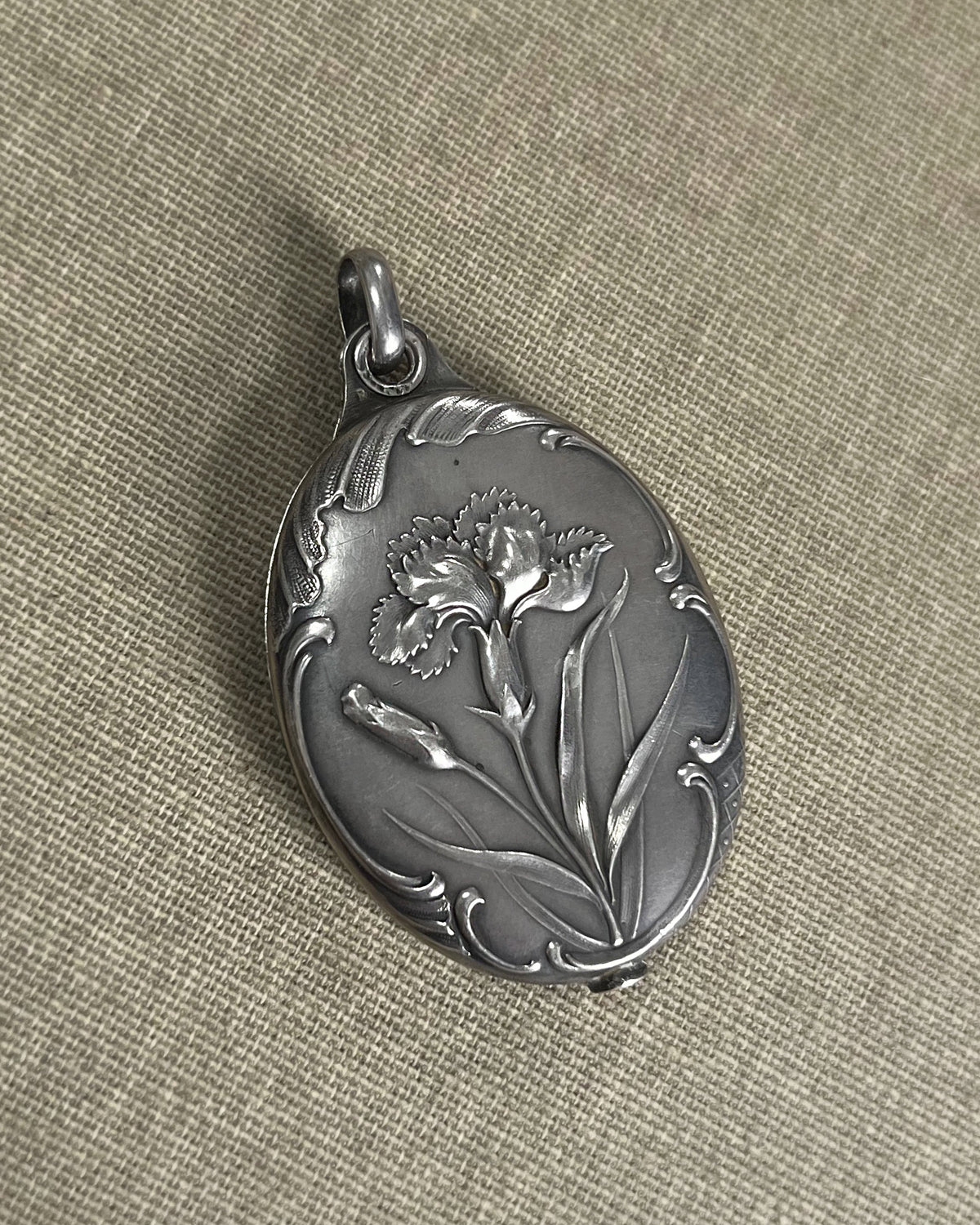 Top view of an antique French Art Nouveau silver iris pocket mirror locket showing the richly chased floral decoration and oval form.