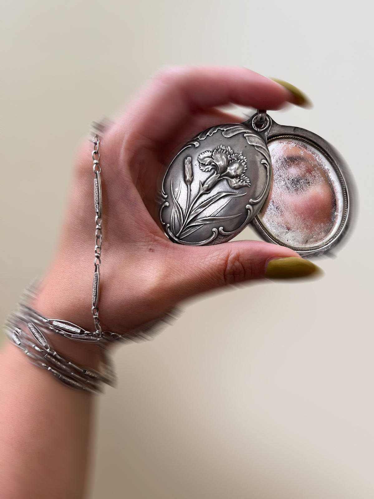 Antique French Art Nouveau silver iris pocket mirror locket shown open in a hand, revealing the two softly aged mirrors inside.