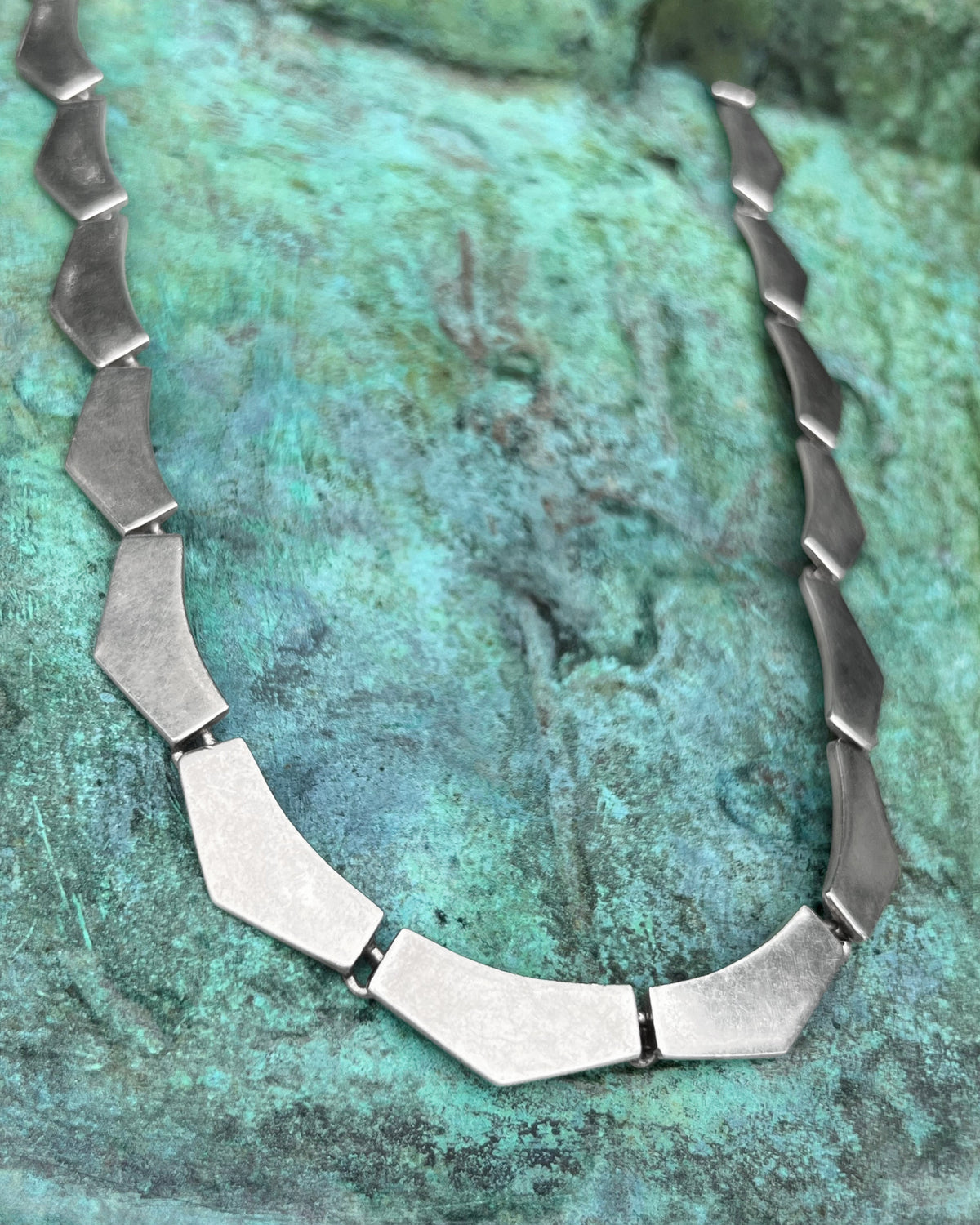 1990s Portuguese vintage Sterling silver Cleopatra necklace with sixteen chunky polished chevron plaques and a rectangular push clasp, shown against a green bronze background.