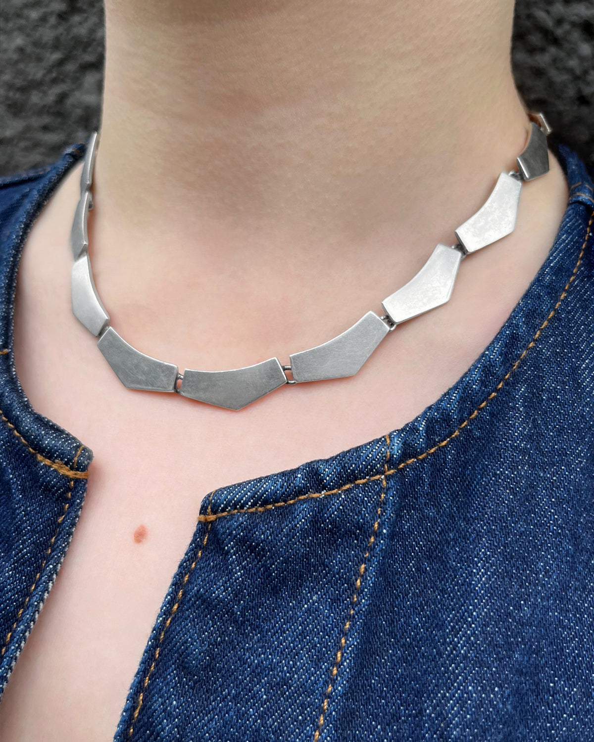 1990s vintage Portuguese Sterling silver Cleopatra necklace with chunky chevron plaques, worn around the neck with a denim top.