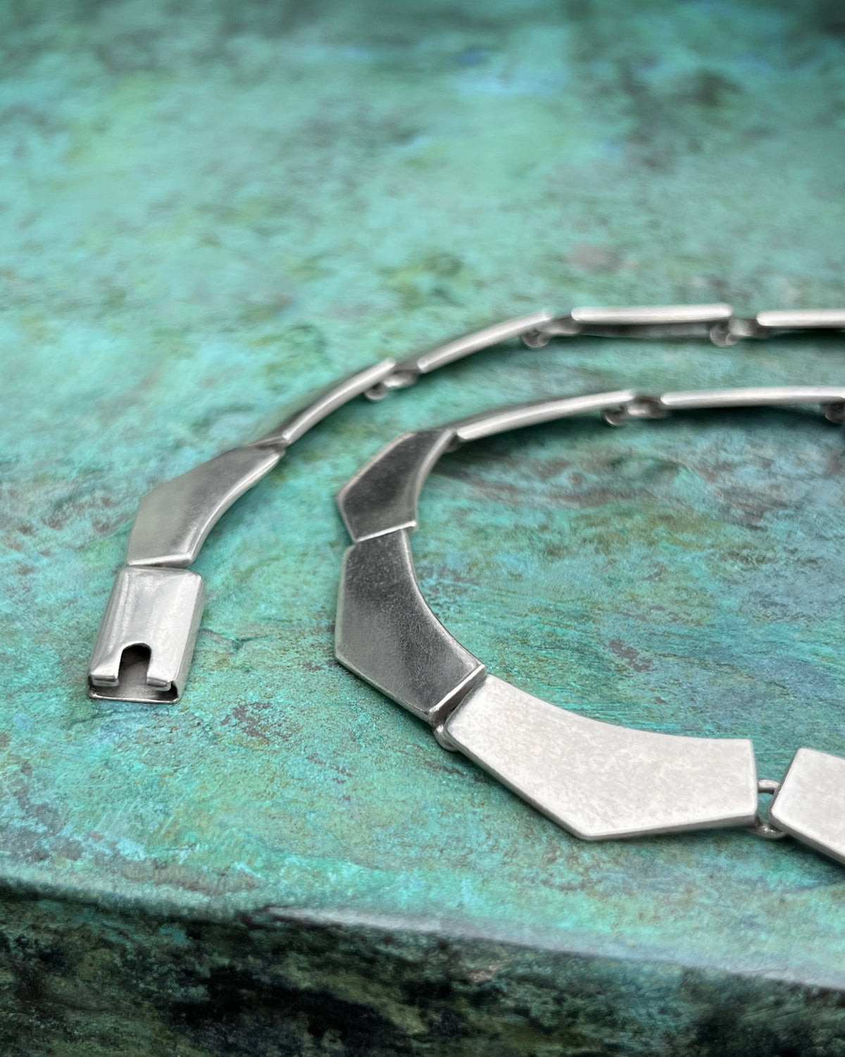 Close-up of the chunky chevron plaques and hidden connecting links on a 1990s Portuguese Sterling silver Cleopatra necklace, shown against a green bronze background.