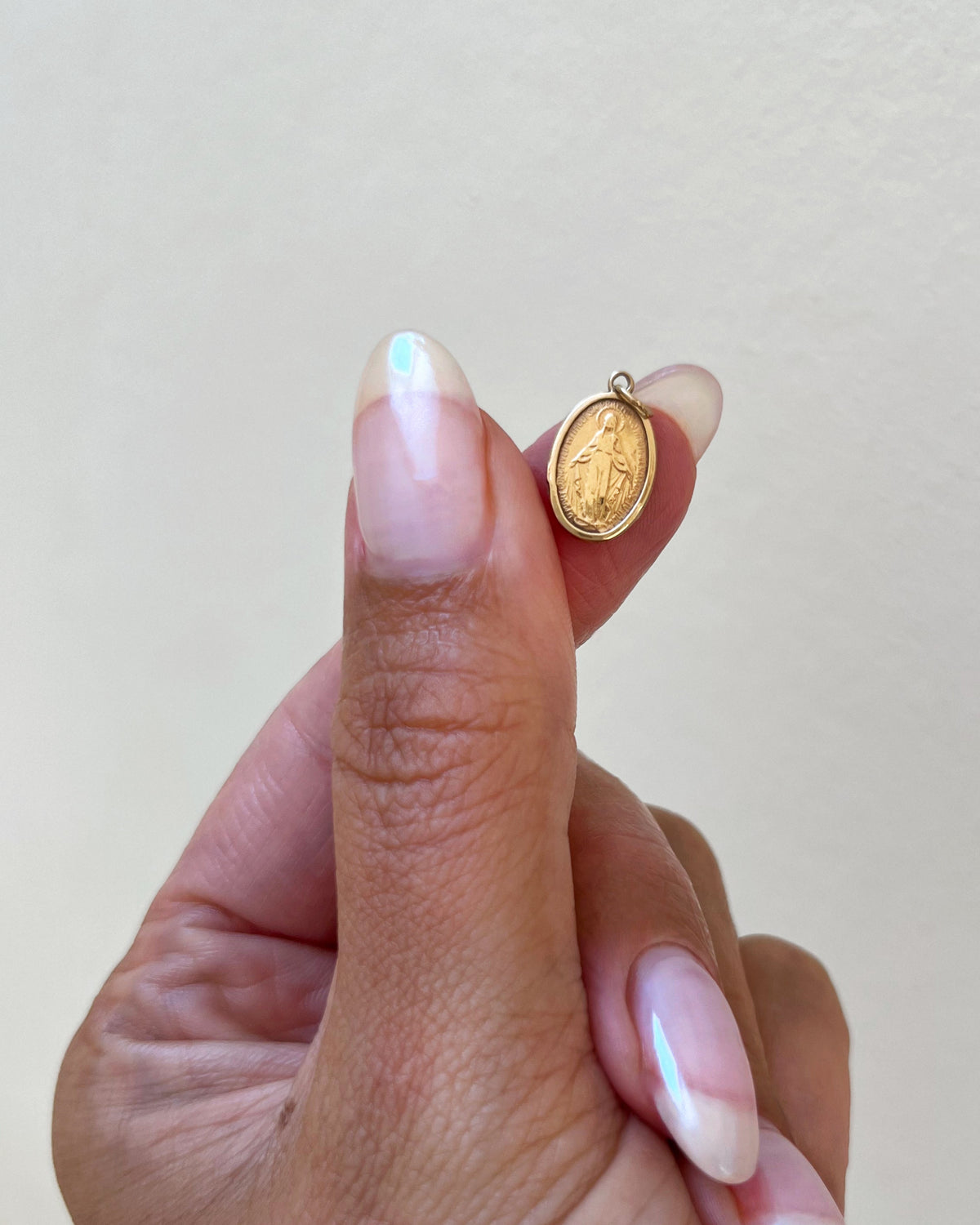 Tiny vintage 9kt yellow gold Miraculous Medal pendant shown on a fingertip to demonstrate its diminutive size.