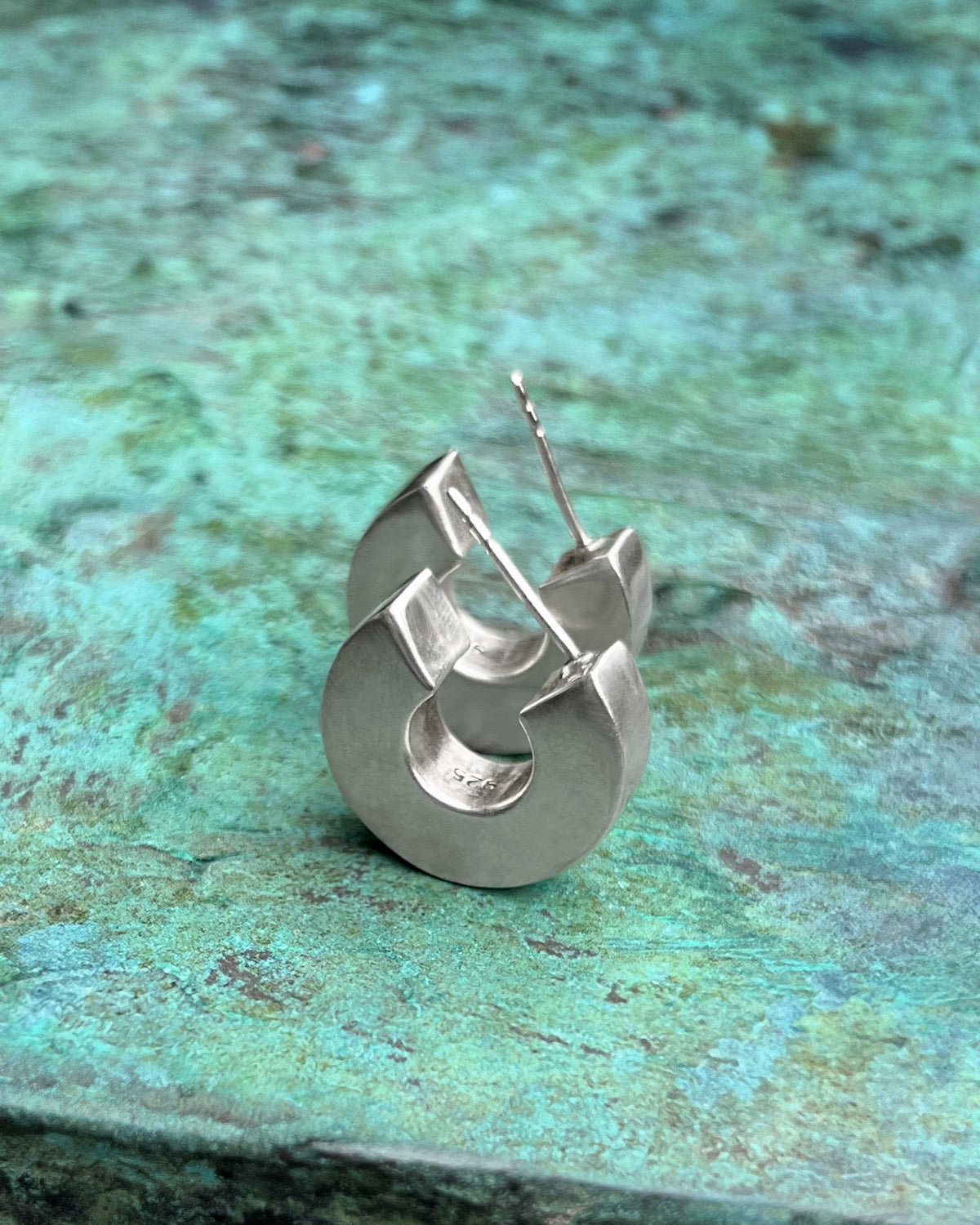 Vintage Sterling silver statement hoop earrings with sharp square edges and polished finish, shown vertically against a green bronze background.