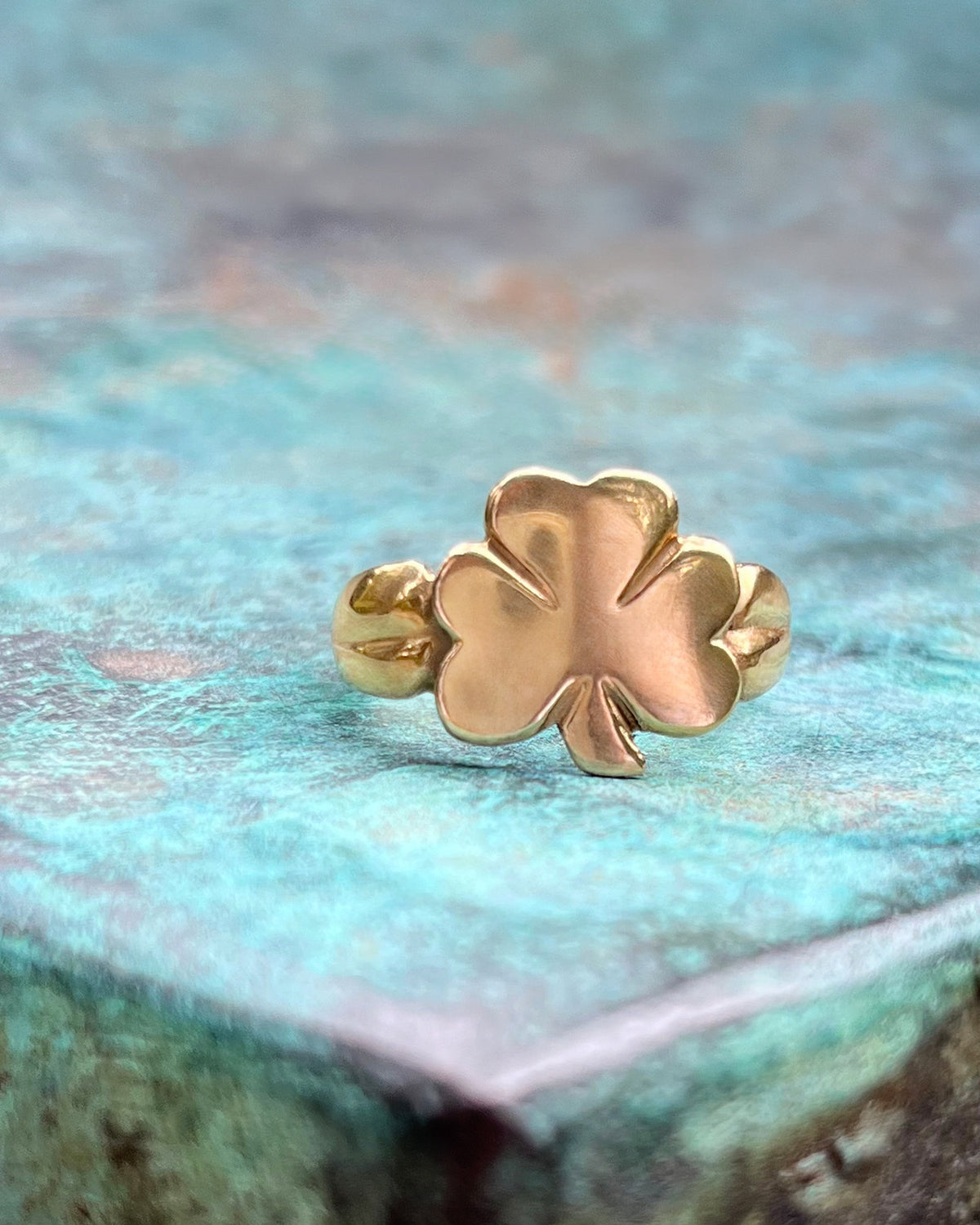 1970s vintage Irish 9kt gold shamrock ring with polished three-leaf clover motif and stylised shoulders, shown against a green bronze background.