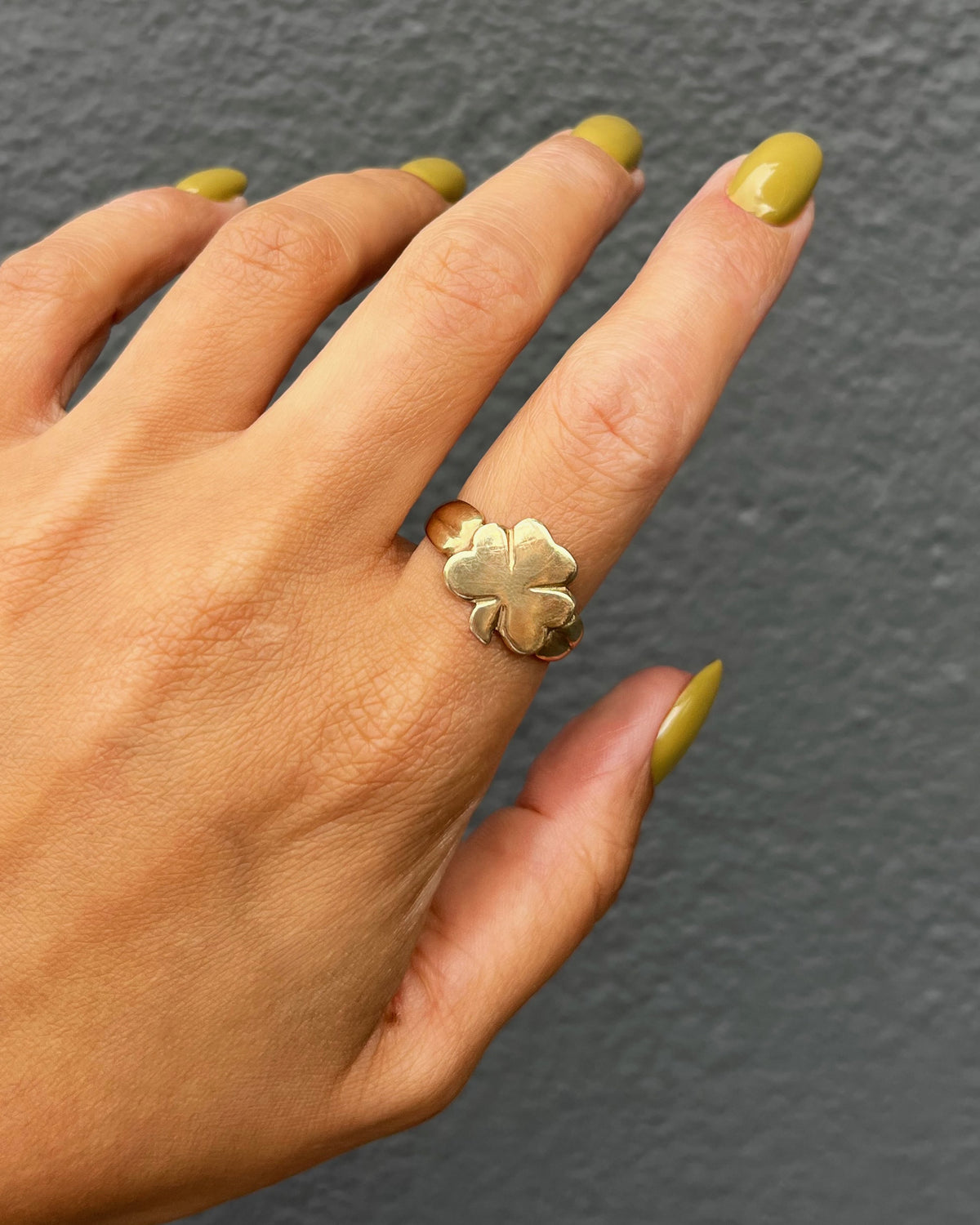 1970s vintage Irish 9kt gold shamrock ring shown worn on a hand against a grey wall.