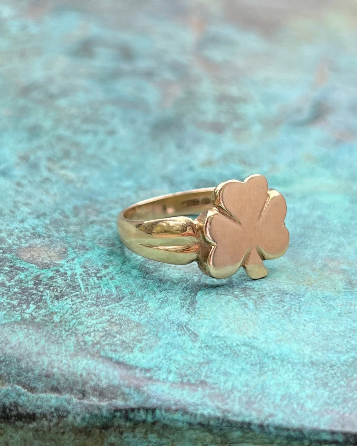 Side view of a 1970s vintage Irish 9kt gold shamrock ring showing the stylised shoulders and profile, against a green bronze background.