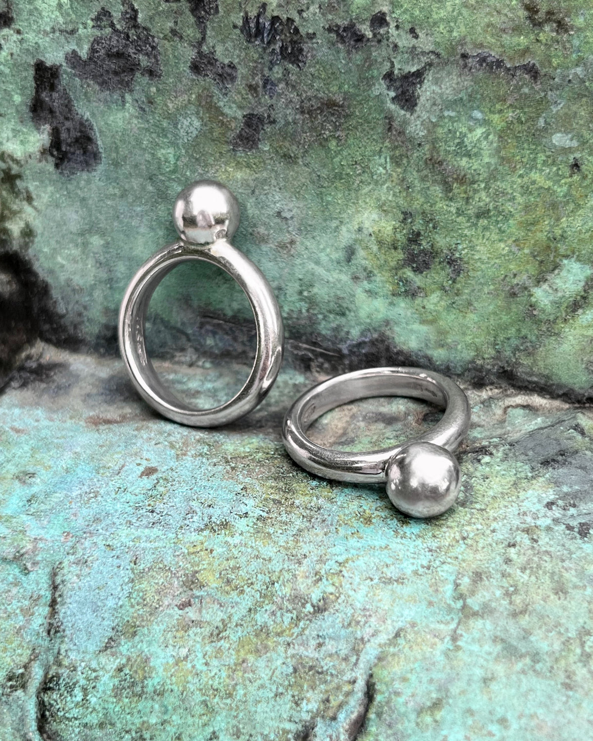Pair of Ti Sento Sterling silver bauble stacking rings shown from the side against a green bronze background.