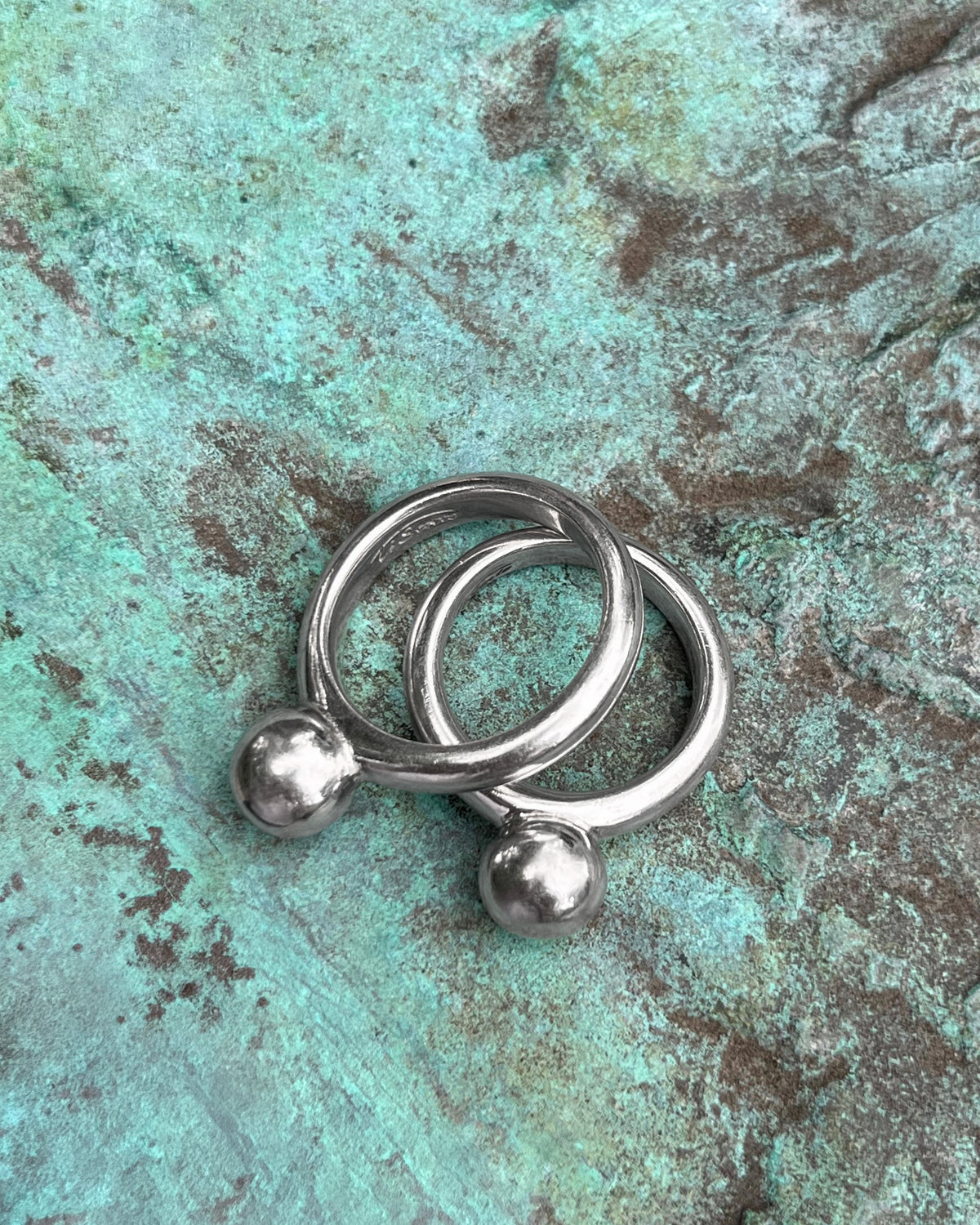 Pair of Ti Sento Sterling silver bauble stacking rings shown from above against a green bronze background.