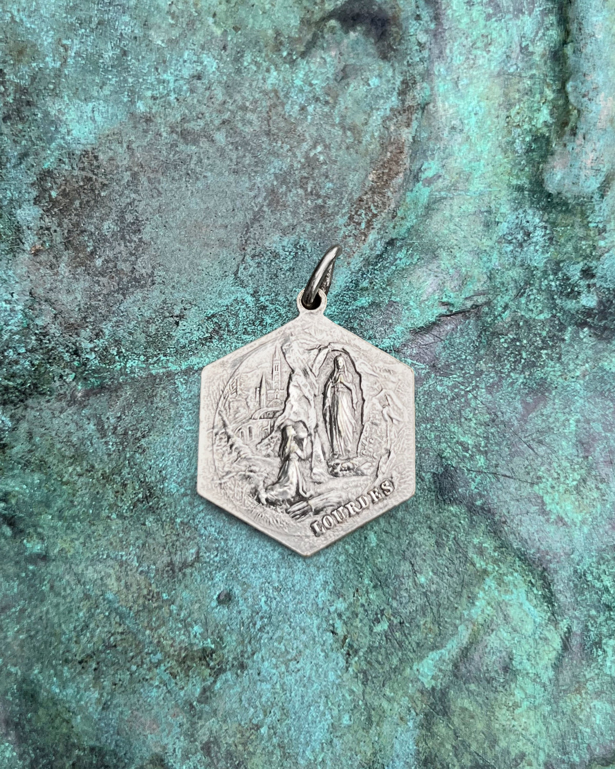Reverse of a French vintage St. Christopher pendant showing the Apparition of the Virgin Mary to Saint Bernadette at Lourdes, against a green bronze background.