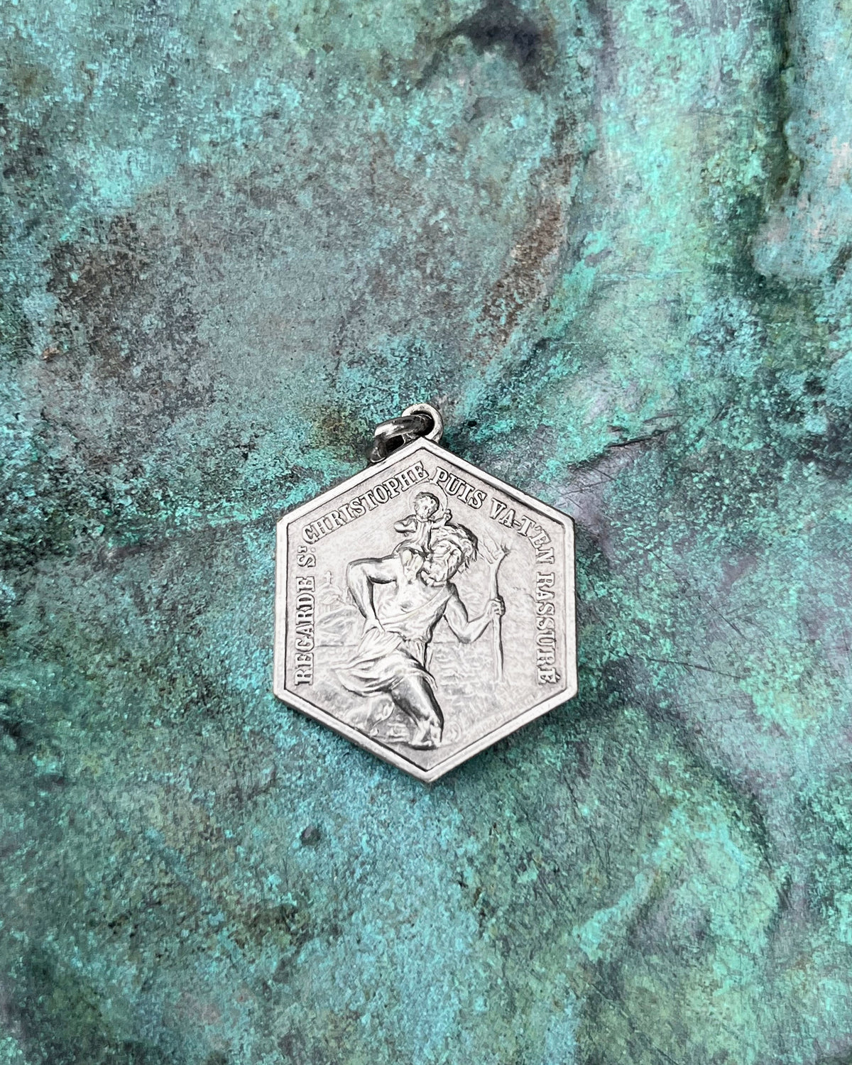 French vintage St. Christopher pendant in a distinctive hexagonal form, depicting St. Christopher carrying the Christ Child through water, shown against a green bronze background.