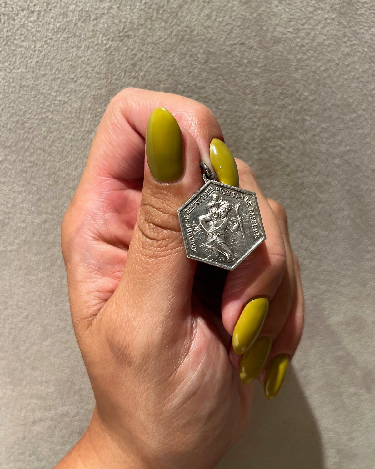 French vintage St. Christopher pendant held in a hand against a grey background, showing the hexagonal form and raised inscription.