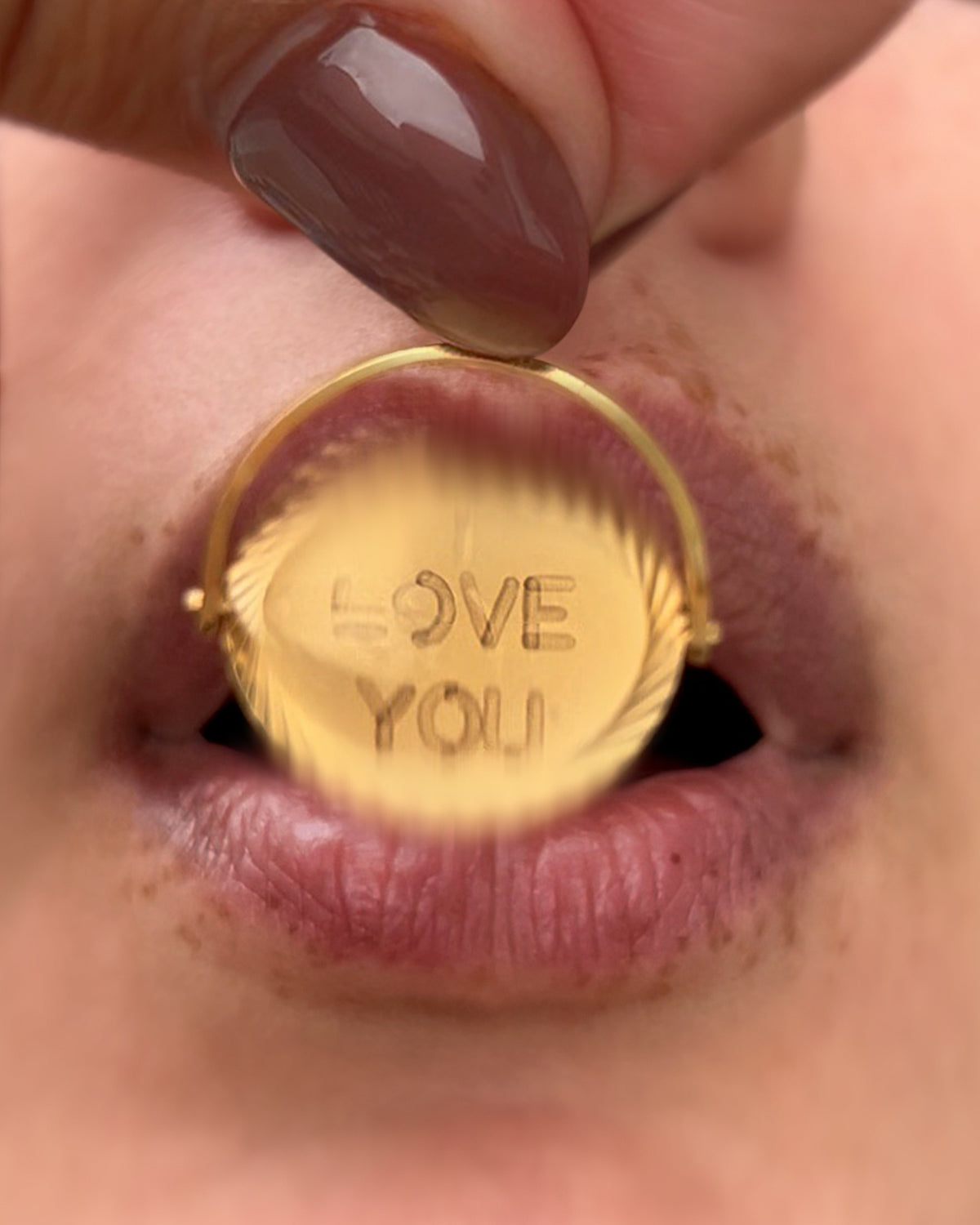 Vintage 1970s 9kt gold “I Love You” pendant being blown to reveal its hidden message, with lips visible in the background.