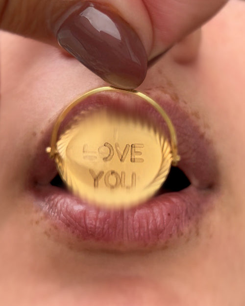 Vintage 1970s 9kt gold “I Love You” pendant being blown to reveal its hidden message, with lips visible in the background.