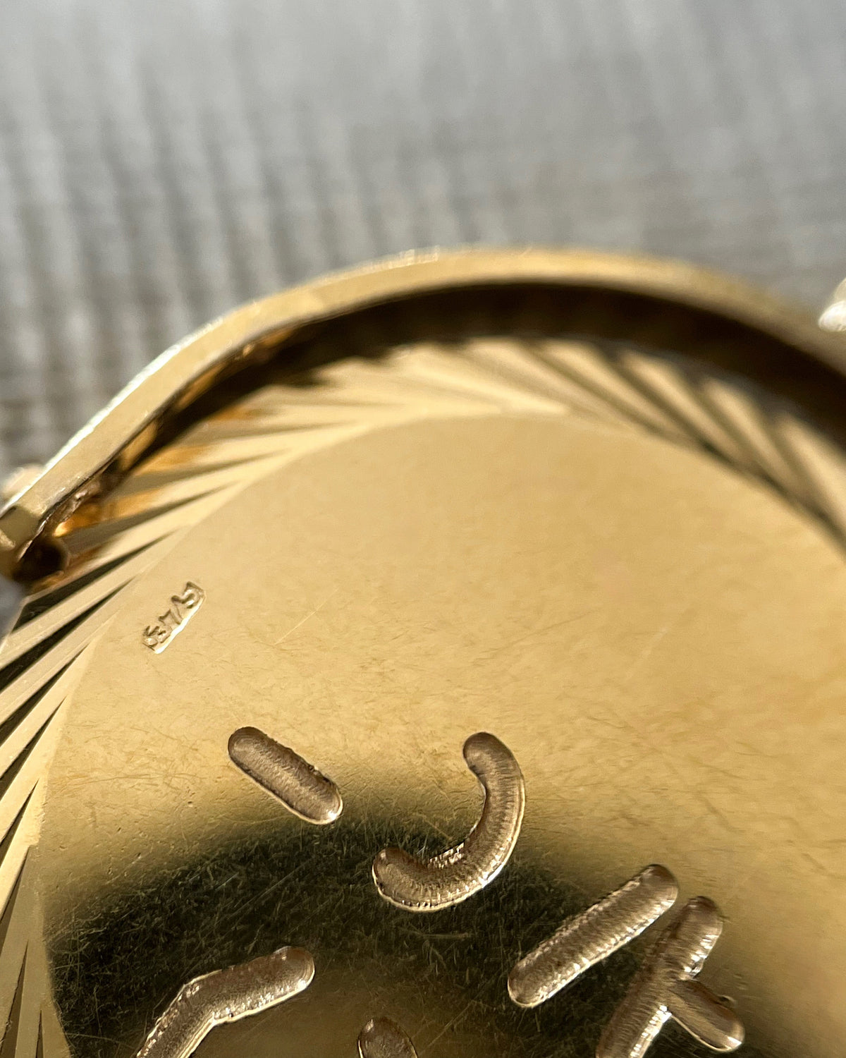 Close-up of the 375 gold hallmark on a vintage 1970s “I Love You” pendant, viewed through a jeweller's loupe.