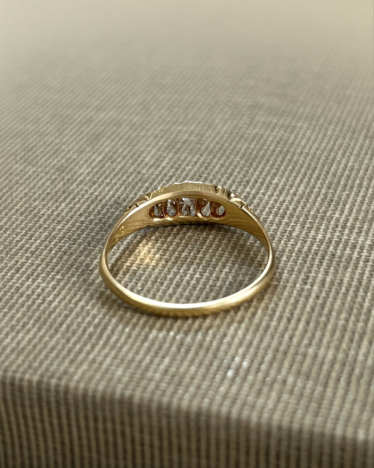 Reverse view of an antique five-stone Old Mine cut diamond ring showing the pierced openwork profile, carved scrollwork and trumpet-shaped shoulders.