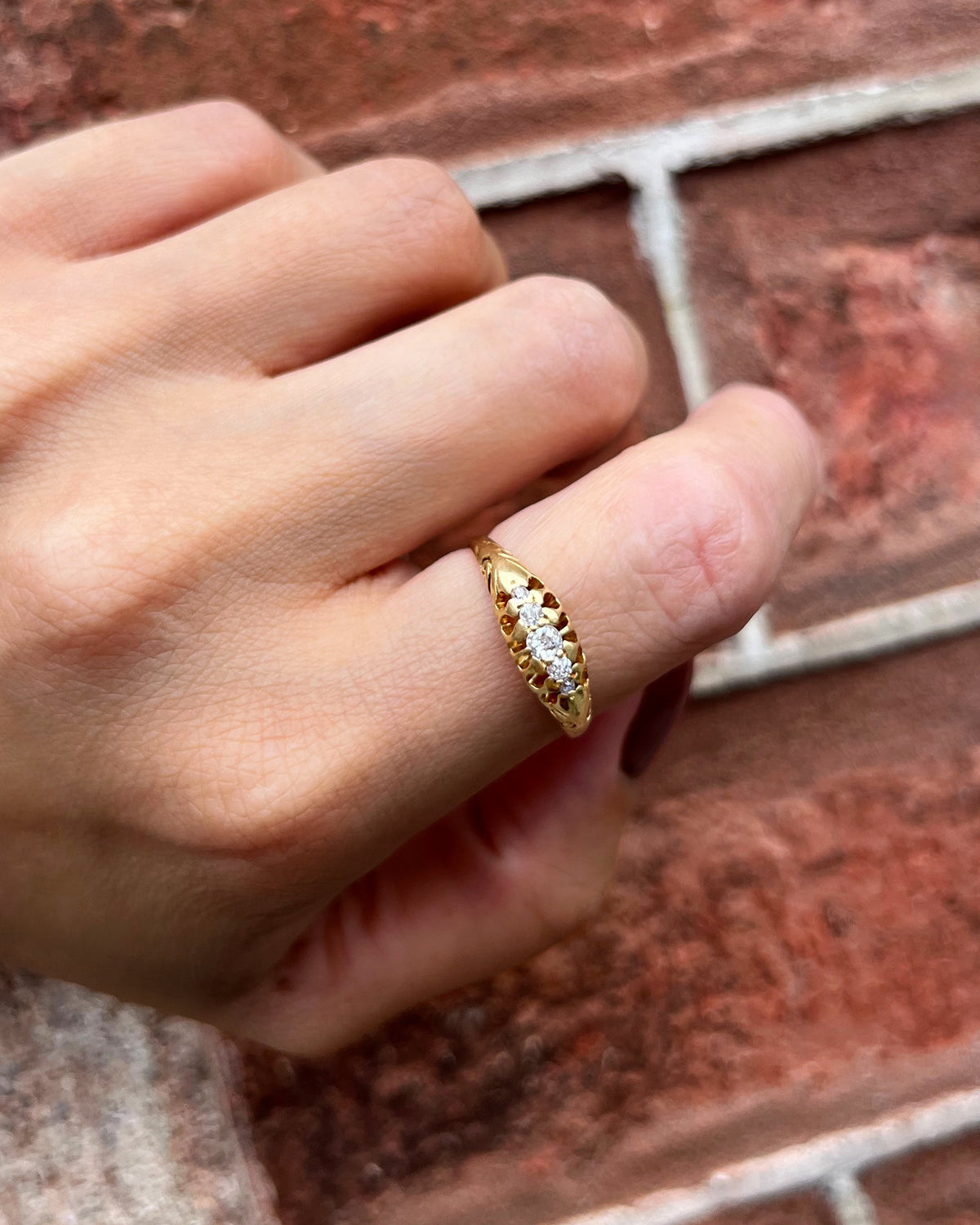 Antique five-stone diamond ring with five graduating Old Mine cut diamonds, shown worn on a hand against a red brick wall.