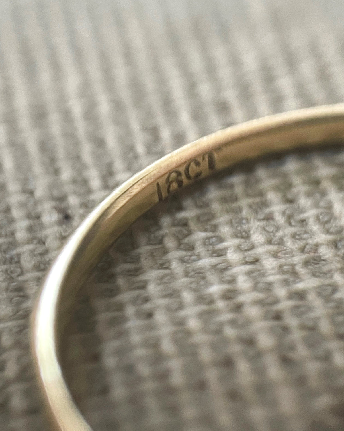Magnified close-up of the 18CT gold mark inside the shank of an antique five-stone diamond ring, viewed through a jeweller's loupe.