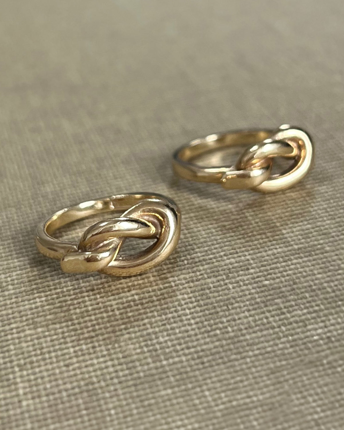 Pair of vintage Irish 9kt gold overhand knot rings shown side by side on textured beige canvas.